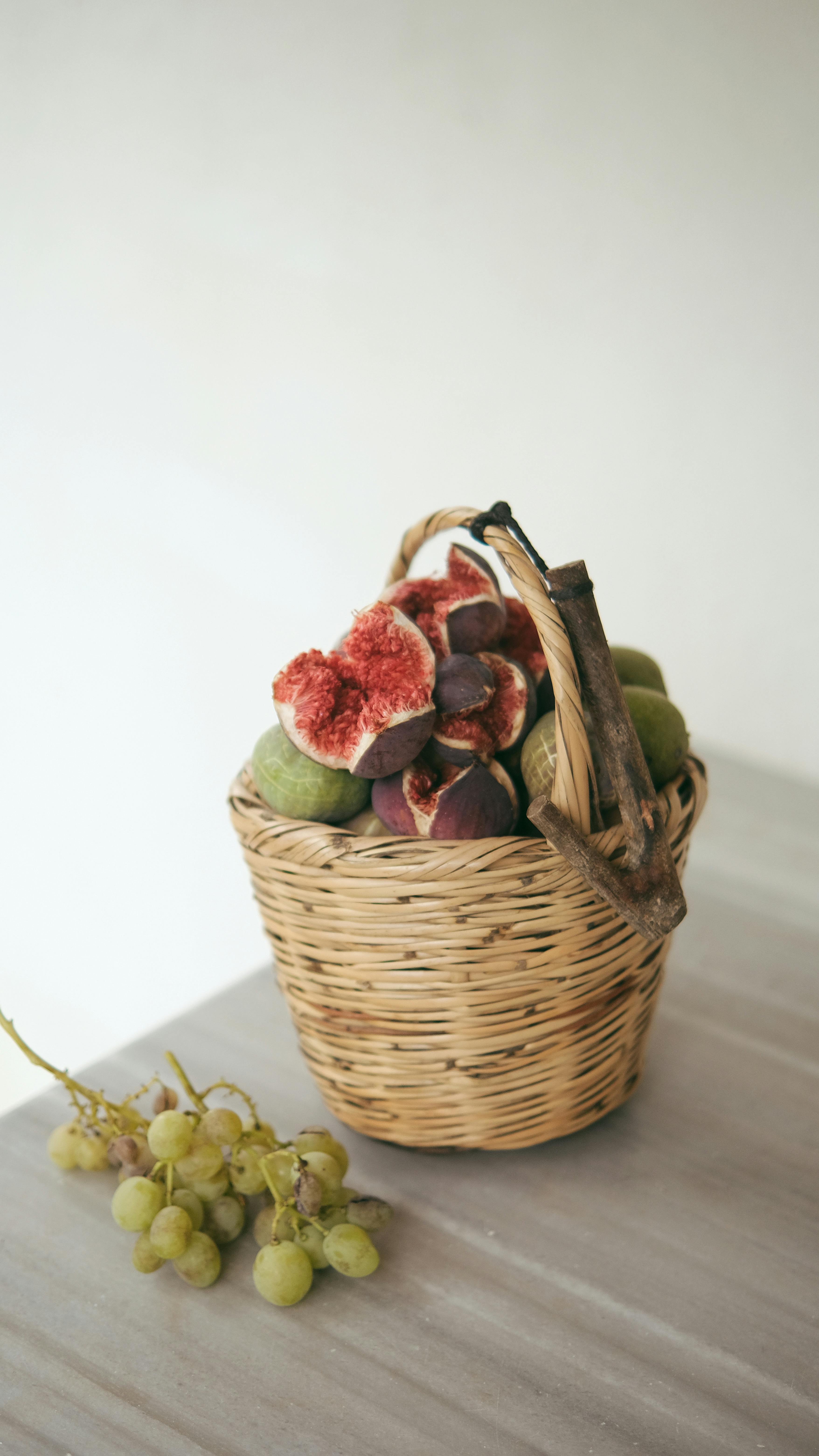 A wicker basket filled with fresh figs and green grapes on a table.