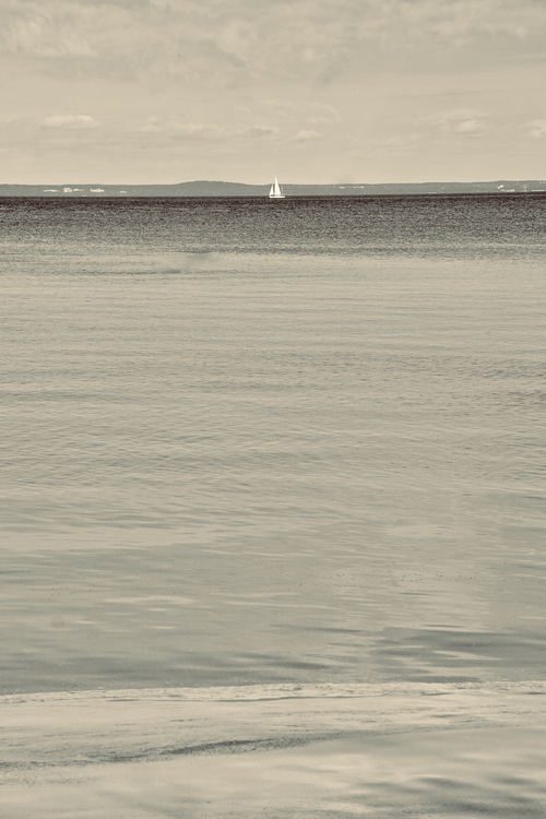 Free Calm sea with a solitary sailboat on the horizon, exuding tranquility. Stock Photo