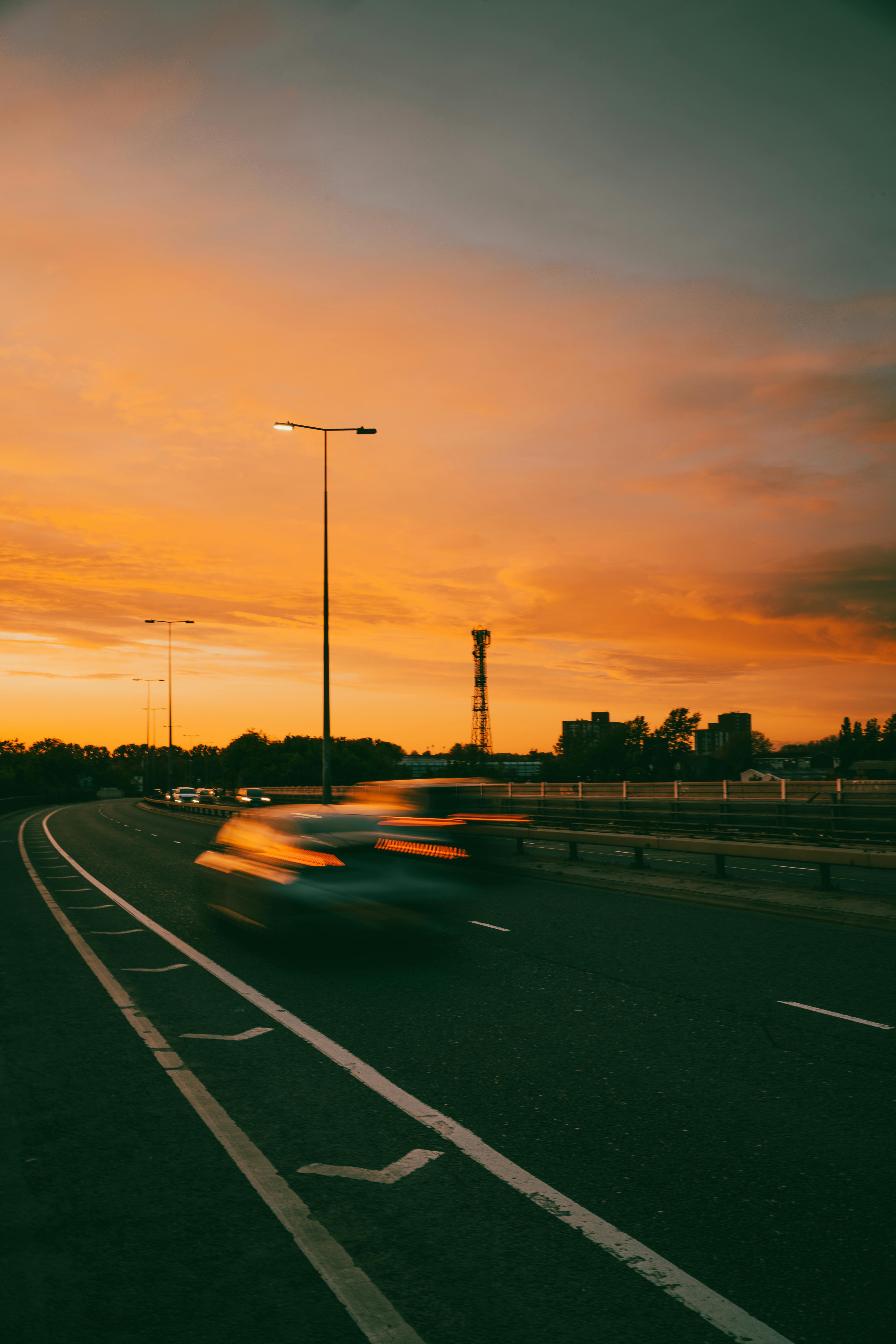 Dynamic scene capturing motion blur of cars on a highway against a vivid sunset sky.