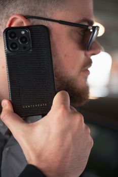 Close-up of a man holding a smartphone with a textured case, indoors.