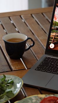 Close-up of a laptop and a cup of tea on a wooden table, creating a cozy workspace vibe.