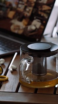 A glass teapot on a wooden table with a laptop in the background, creating a cozy workspace vibe.