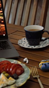 A warm indoor scene of a laptop, cup of tea, and snack on a wooden table.
