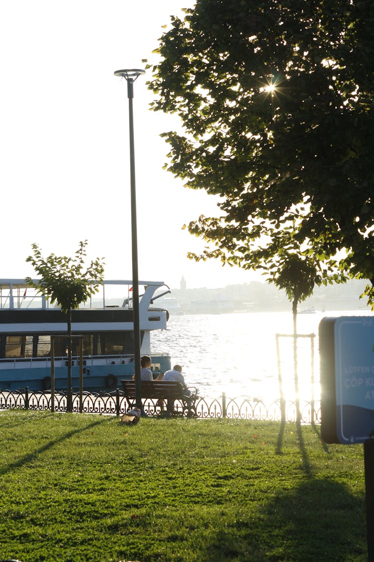 Two People Sitting By The Water At Sunset 