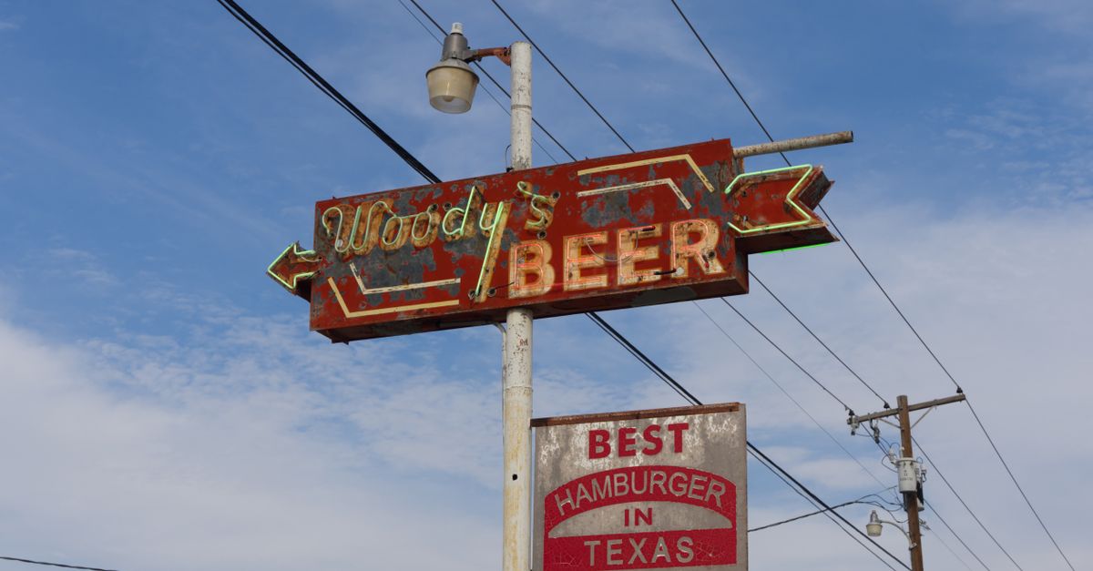 Rusty vintage Woody's Beer sign against a clear blue sky in Mineral Wells, Texas.