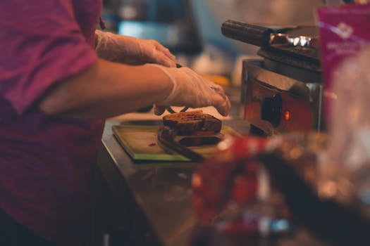 A chef wearing gloves prepares a sandwich indoors with professional equipment.