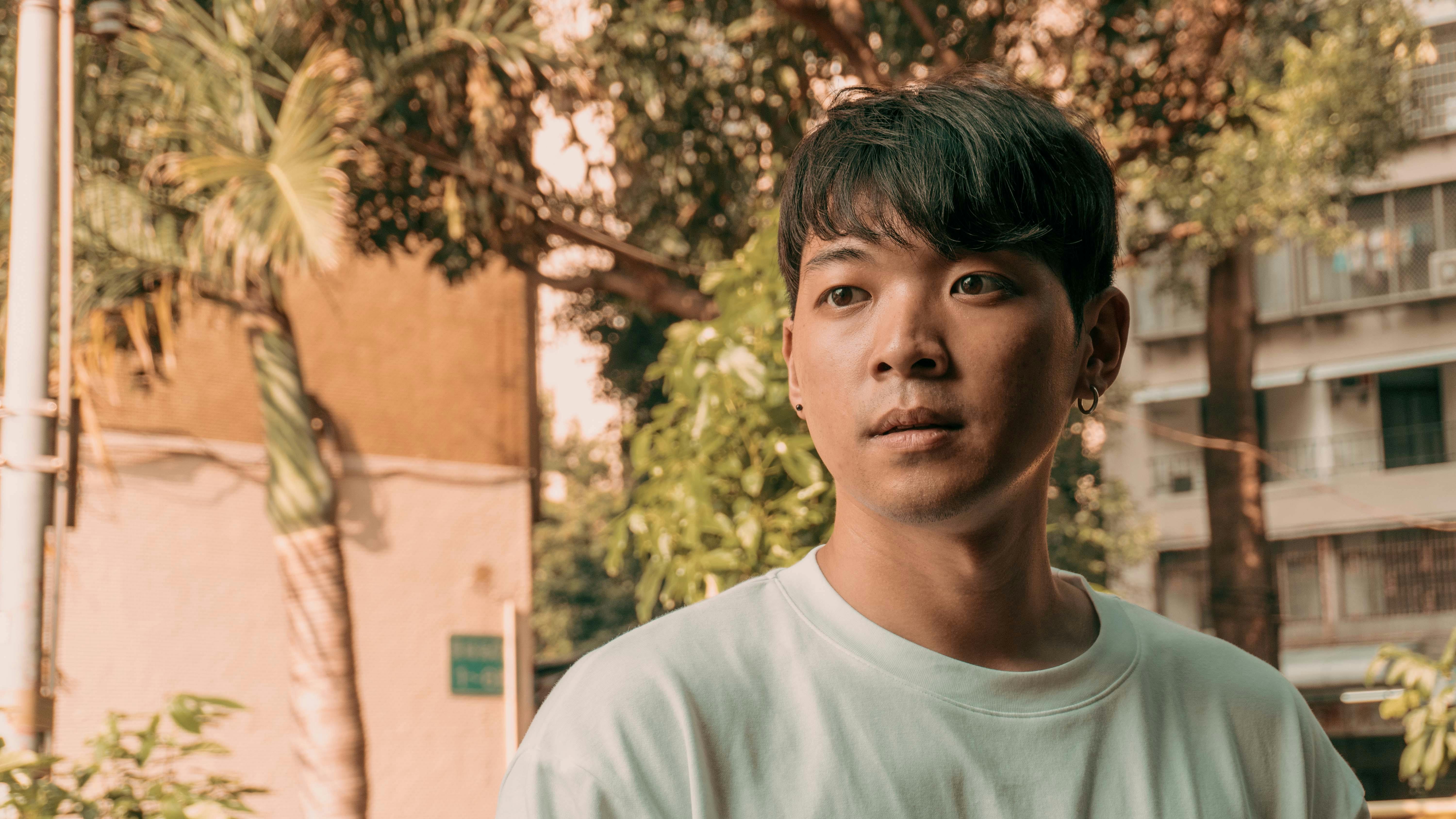 Portrait of an Asian man with short black hair in a sunlit urban setting.