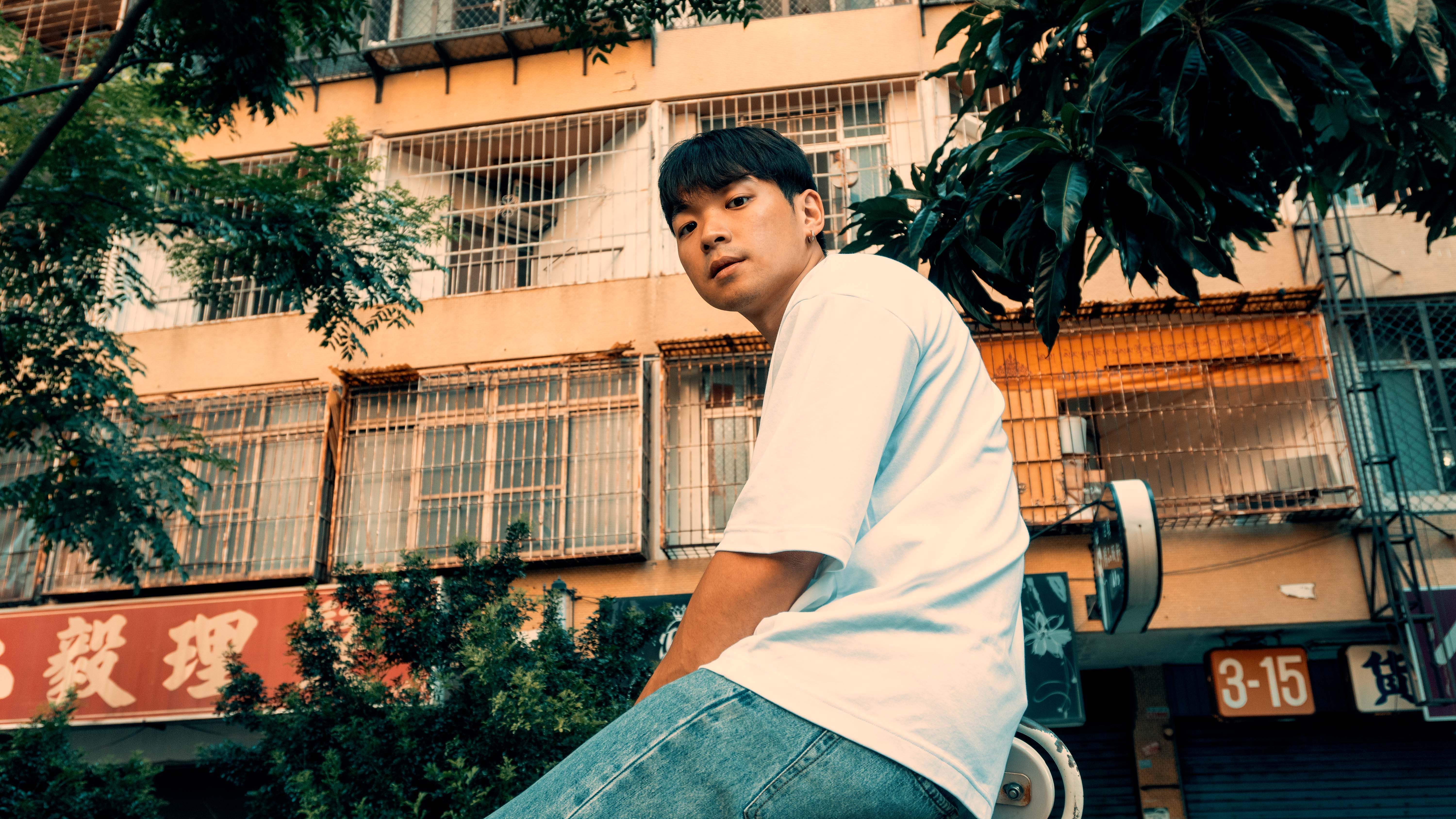 Asian man sitting on a scooter in front of urban building during daytime.