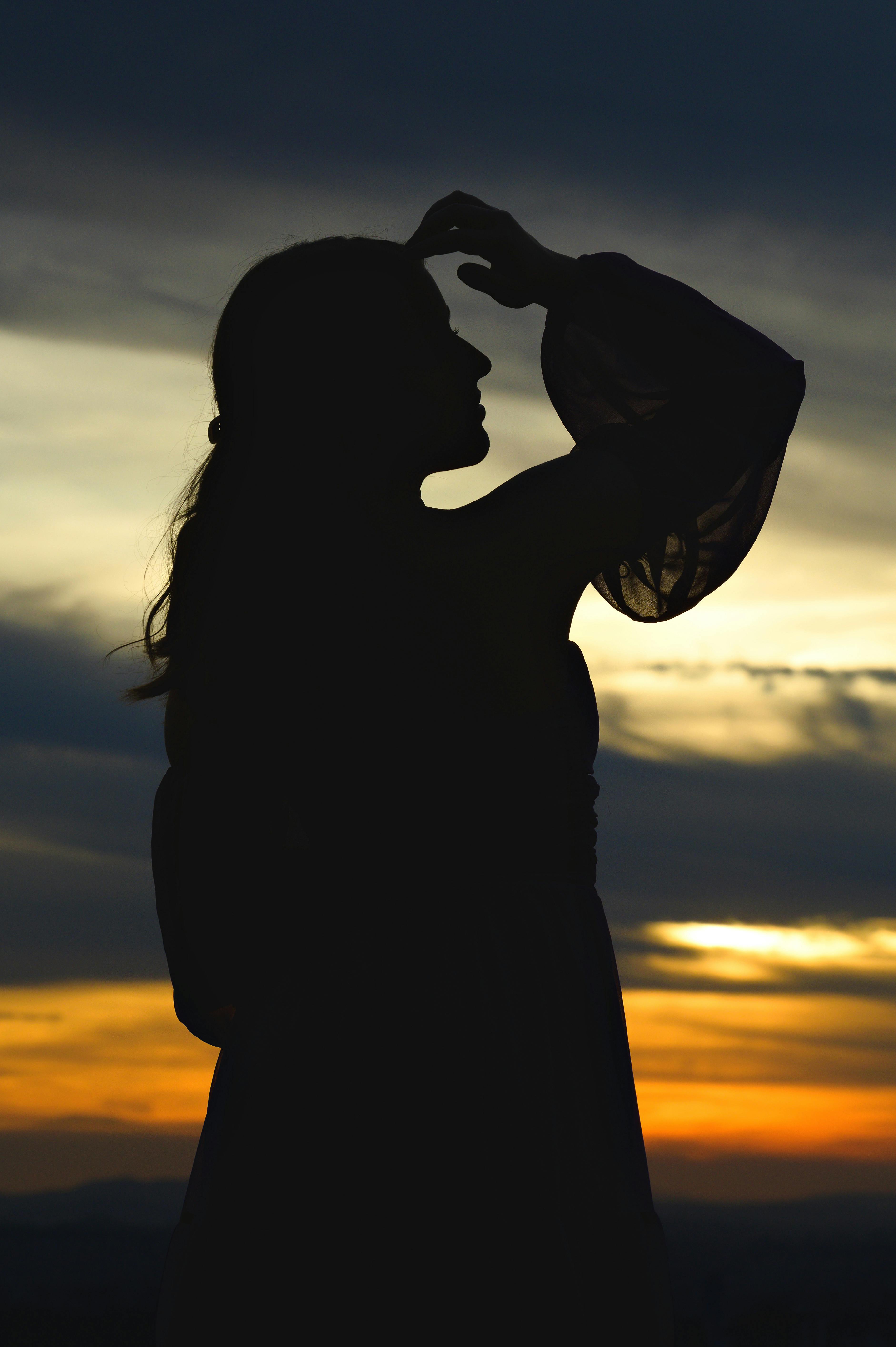 A silhouette of a woman with hand on forehead against a sunset sky, evoking calm and contemplation.