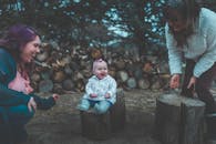 婴儿在户外的原木旁与家人一起玩耍，脸上洋溢着微笑