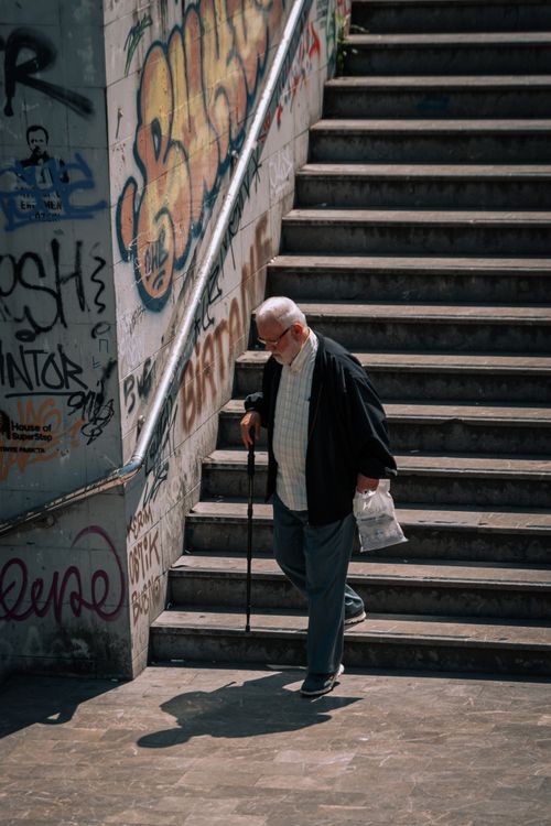 Free Elderly man with cane descends graffiti-covered stairs in urban setting. Stock Photo
