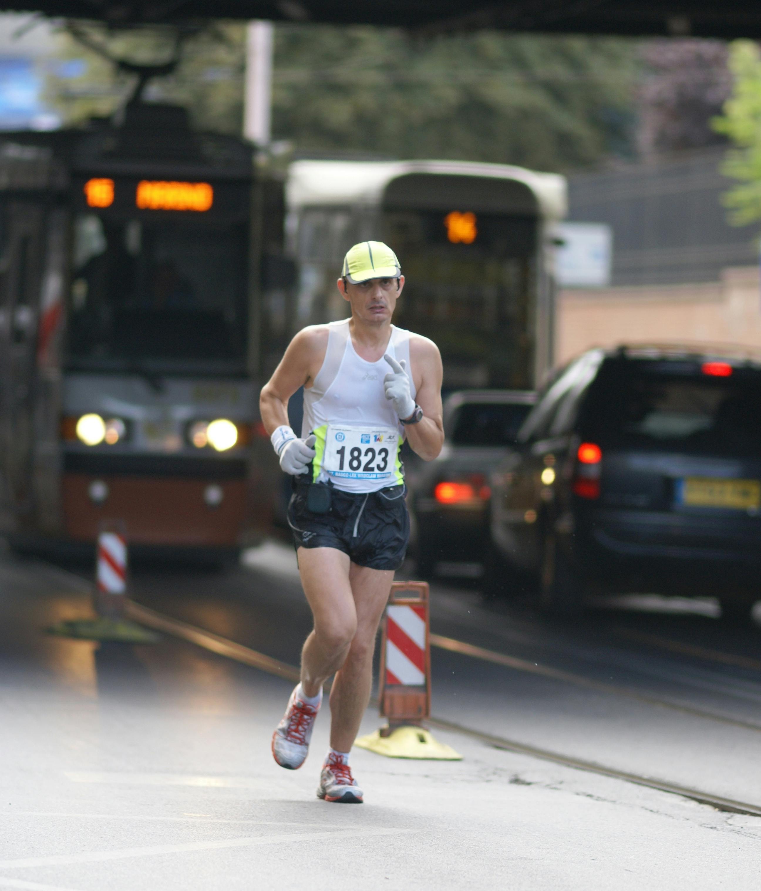 Man running a marathon on city streets with traffic and trams in the background.