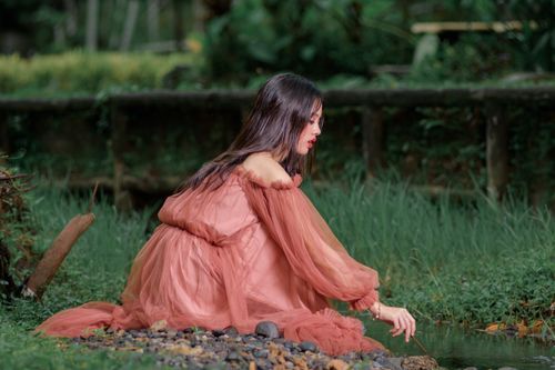 Free A woman in a flowing dress enjoying the tranquility by a stream in a lush outdoor setting. Stock Photo