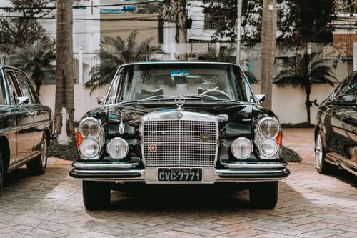Free Classic black vintage car parked outdoors surrounded by greenery, capturing an elegant urban vibe. Stock Photo