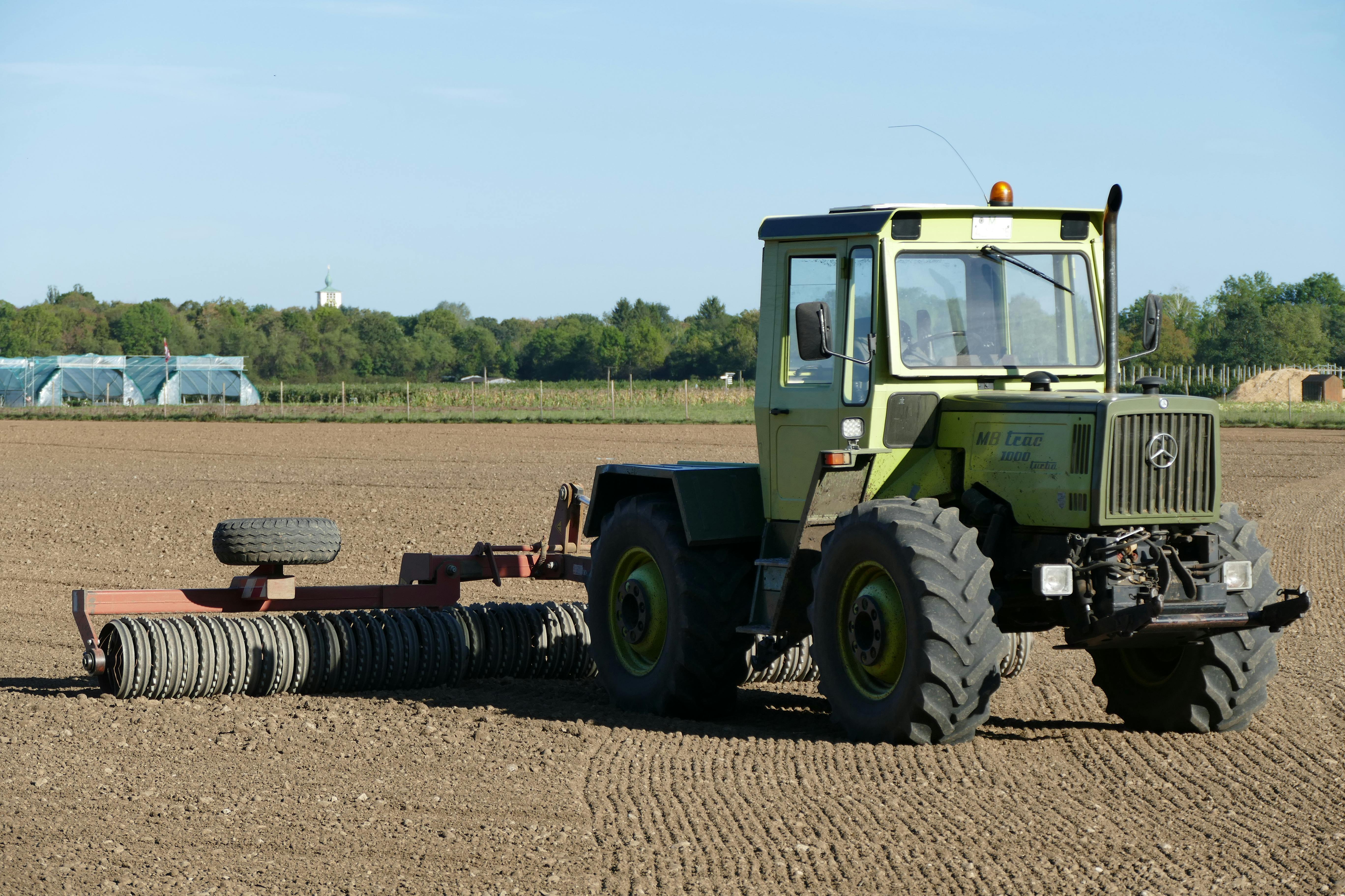 Green tractor preparing a field for planting in rural München, Germany. Clear blue skies.