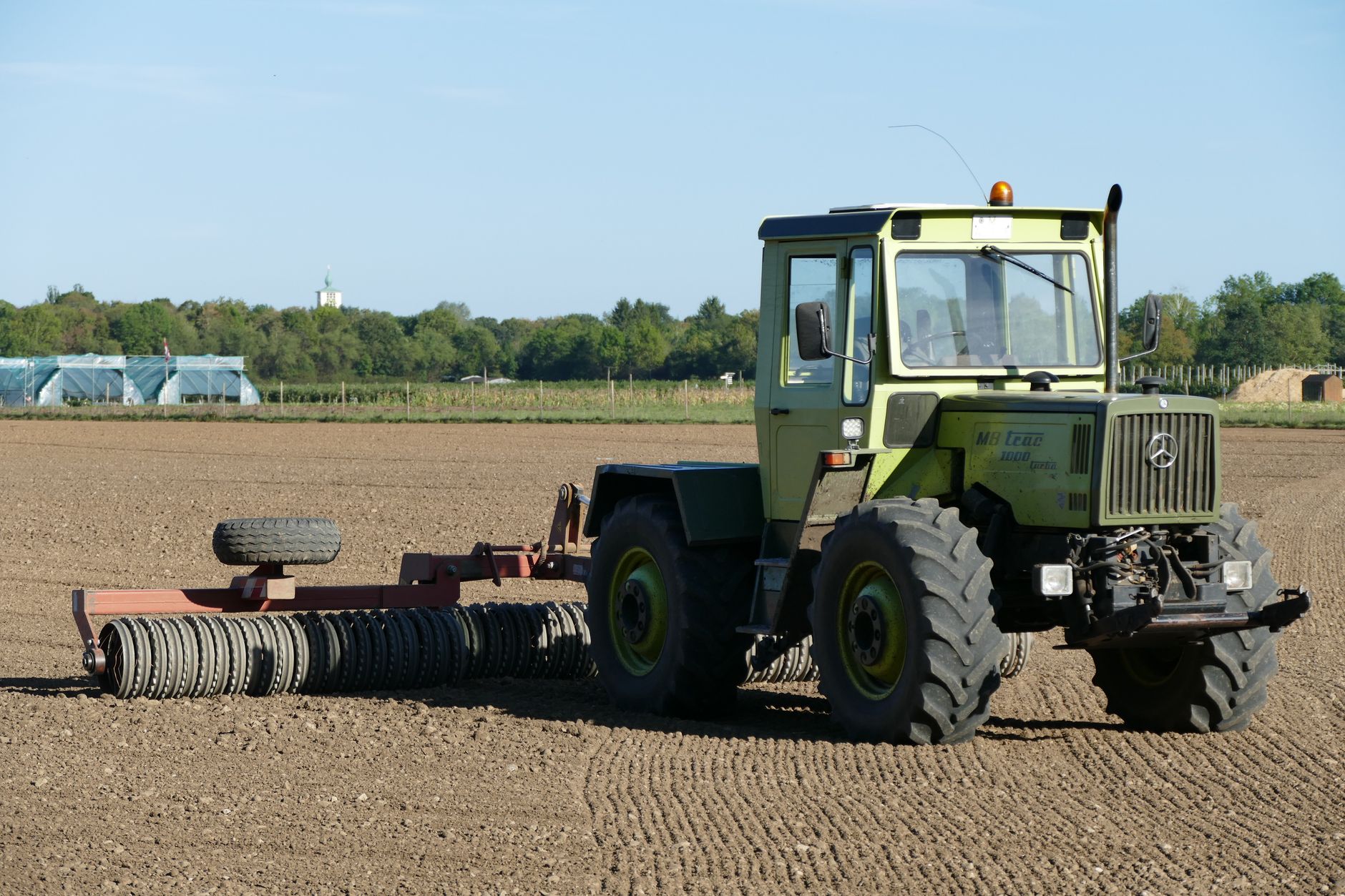 Green tractor preparing a field for planting in rural München, Germany. Clear blue skies.