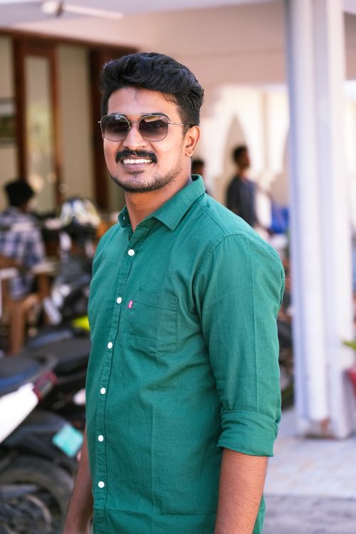 Free Smiling man in a green shirt wearing sunglasses, enjoying a sunny day outdoors. Stock Photo