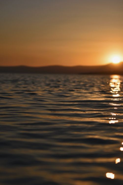 Free Calm lake waters reflecting a beautiful sunset sky with gentle waves. Stock Photo