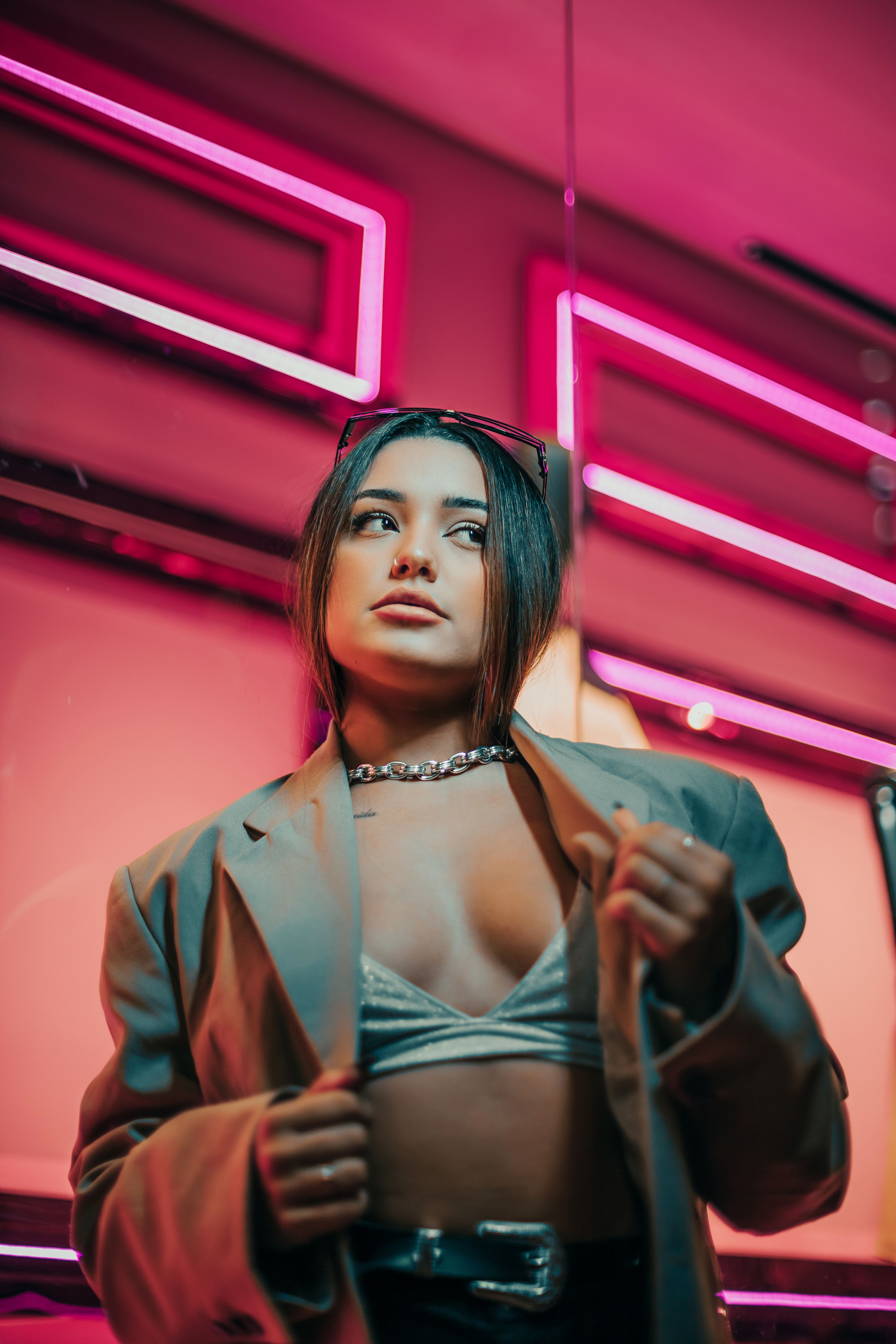 Mulher antenada na moda posa com confiança sob luzes neon rosa em ambiente urbano.