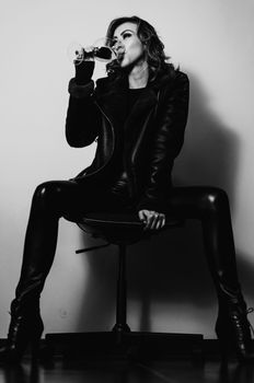 Fashionable woman in black leather sitting and drinking wine in a monochrome style.