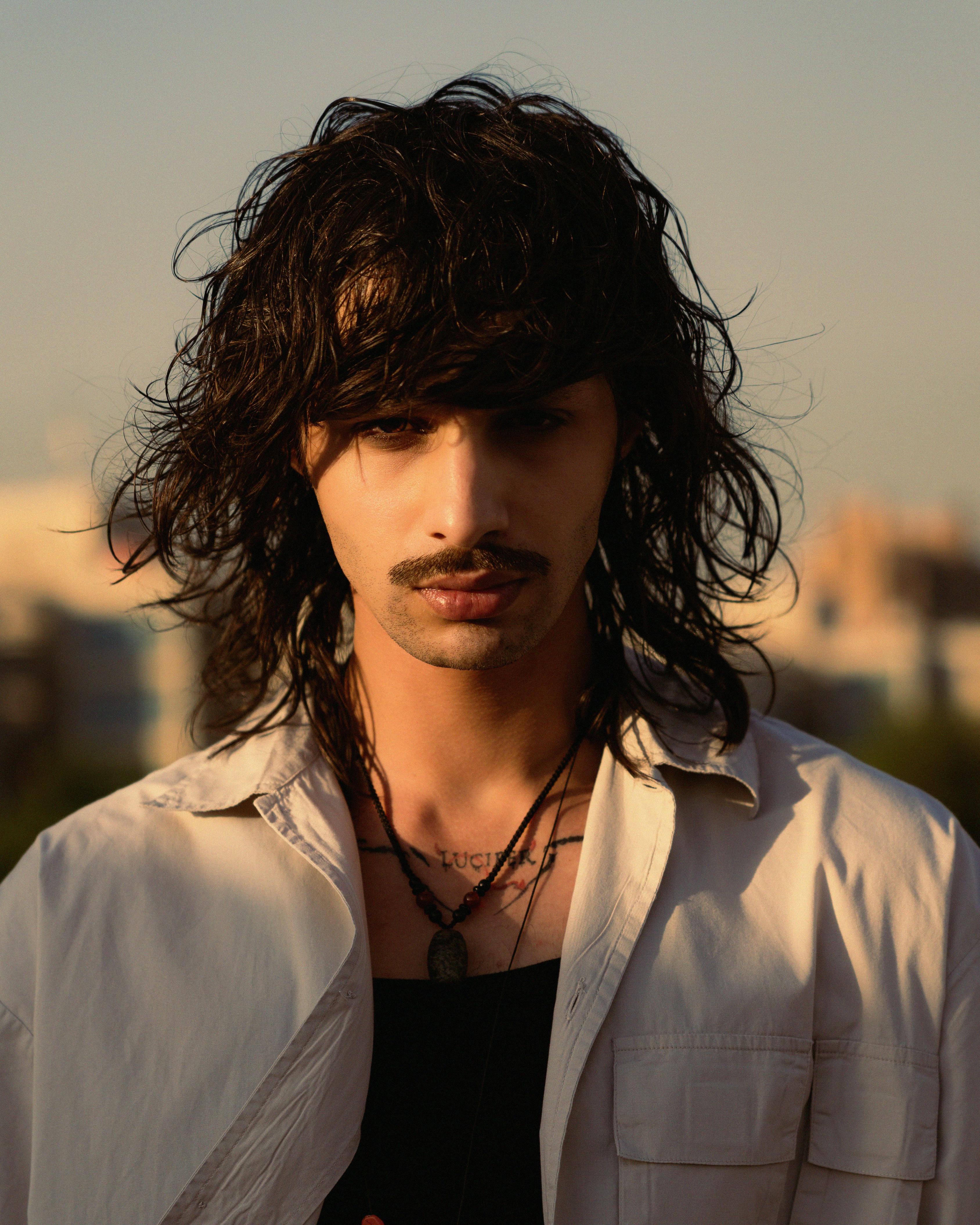 Captivating portrait of a young man with tousled hair and mustache in Iraqi sunlight.