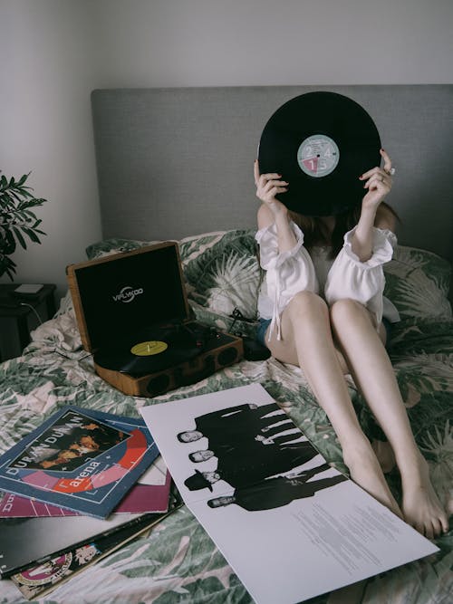 Woman Sitting on the Bed with a Record Player and Vinyl Records 