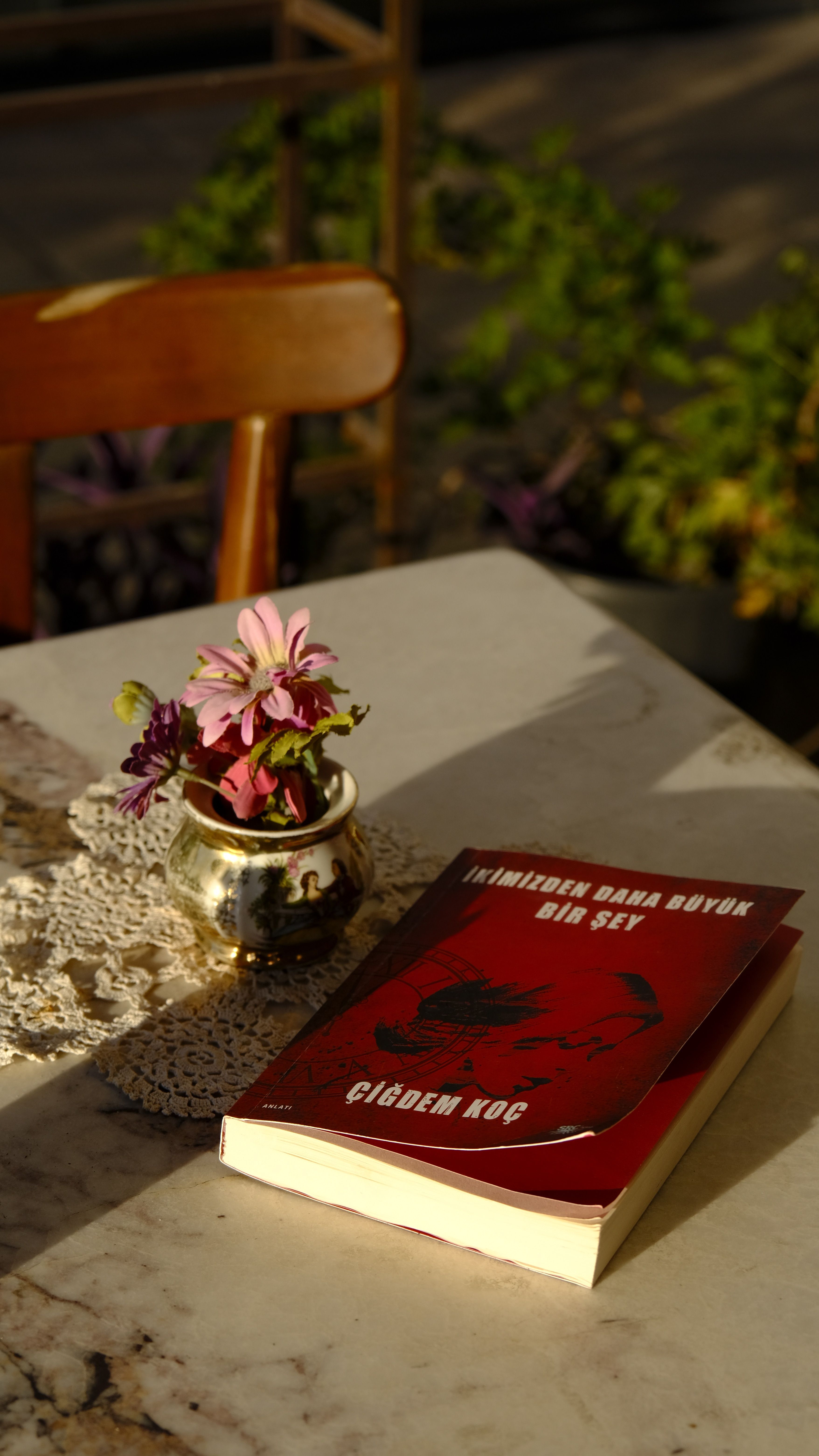 A book and flowers on a sunlit table create a serene ambiance.