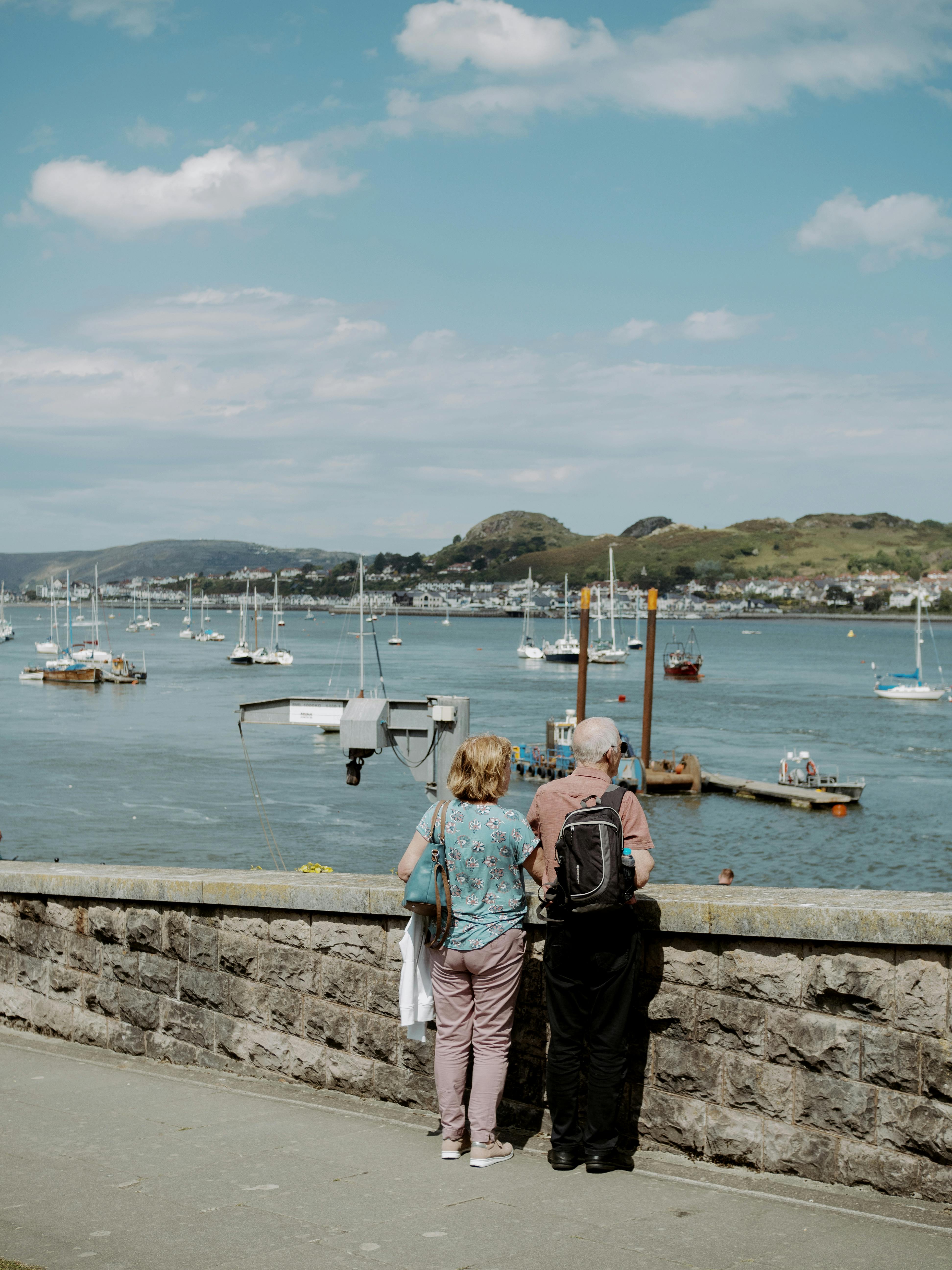 A senior couple takes in a scenic view of the sea from an urban wall, enhancing leisure and travel mood.