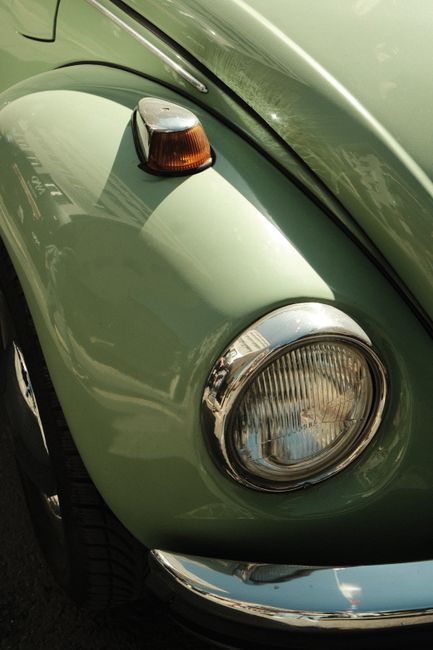 Close-up of a vintage light green Volkswagen Beetle headlight and fender.