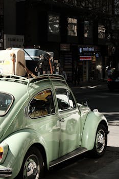 A classic green Beetle parked in an urban setting with suitcases on the roof, evoking a retro travel vibe.