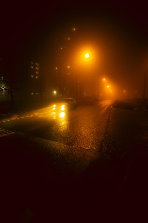 Free Car headlights illuminate a foggy city street at night, creating a moody atmosphere. Stock Photo