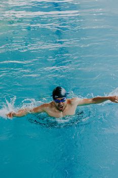 Adult swimmer in a swim cap practicing strokes in an indoor pool.
