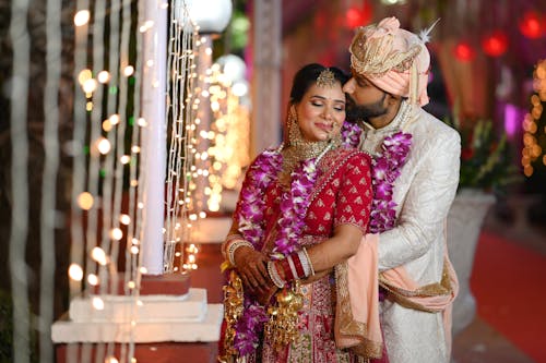 Smiling and Kissing Newlyweds in Traditional Clothing with Garlands