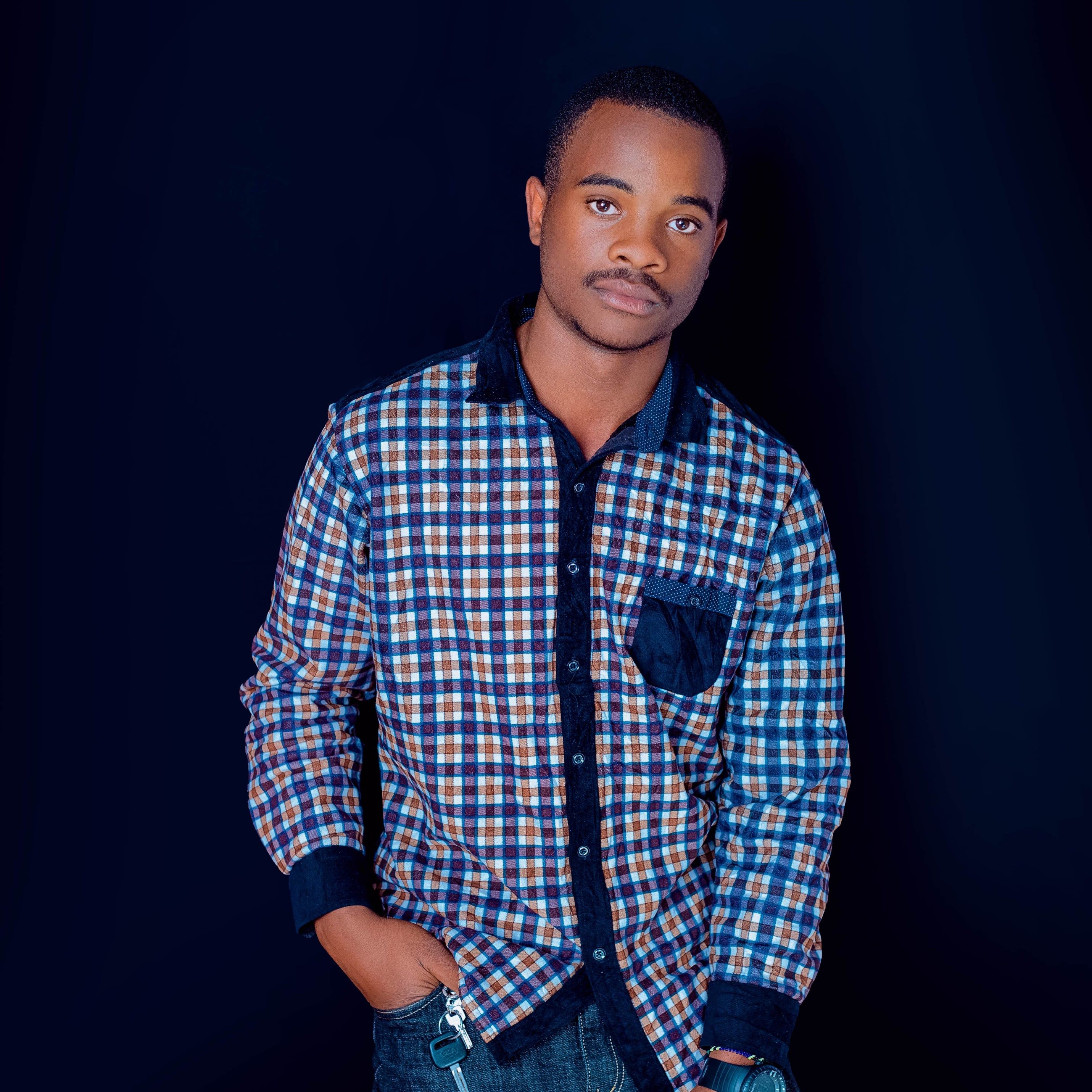 Young man with a plaid shirt posing confidently against a black backdrop.