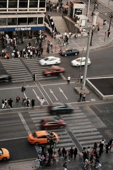 A bustling city intersection with blurred motion of cars and people waiting to cross.