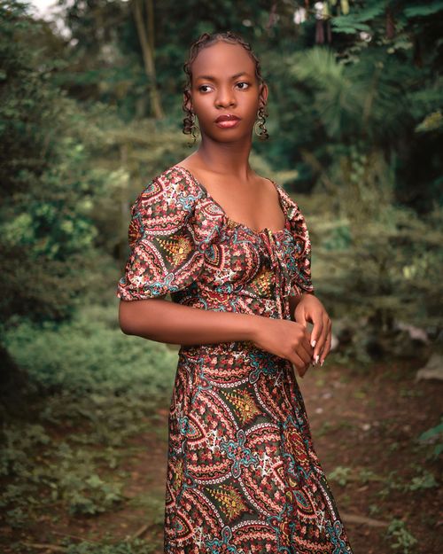 Free A woman in a vibrant patterned dress poses elegantly in a lush forest setting, capturing summer vibes. Stock Photo