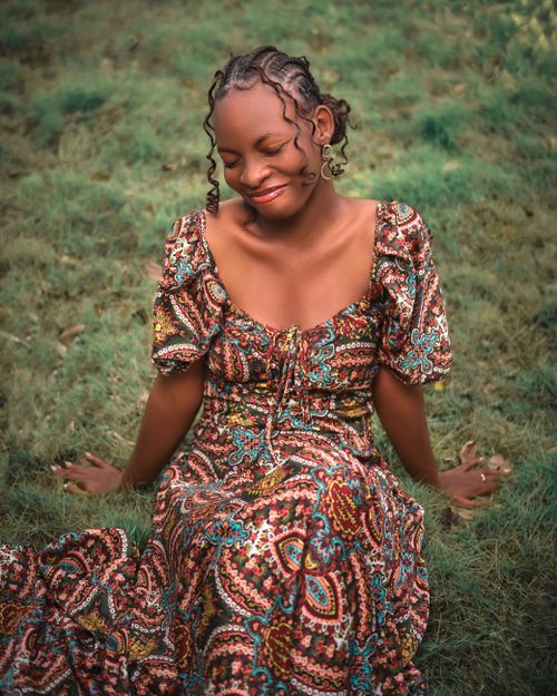 Free Portrait of a smiling woman in a colorful dress sitting outdoors on grass. Stock Photo