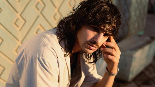 Free A young man with long hair and a mustache sits in deep thought outdoors, highlighting his unique style. Stock Photo