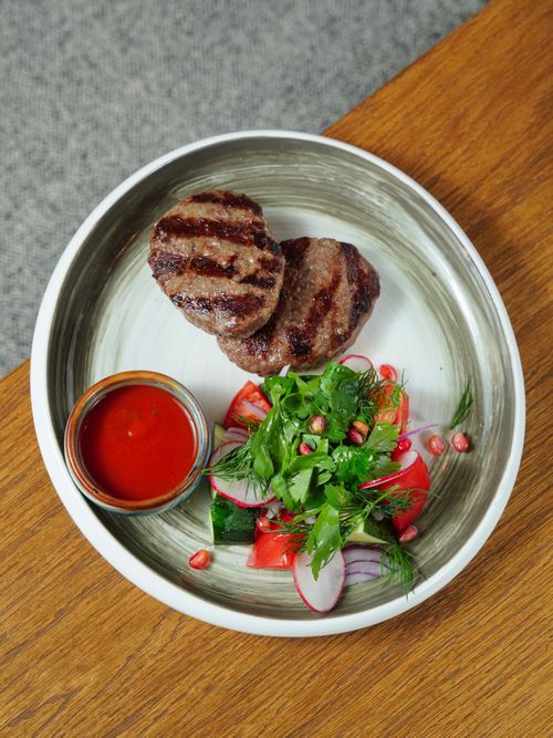 Free Top view of grilled meat patties with fresh vegetable salad and red sauce in a ceramic bowl. Stock Photo