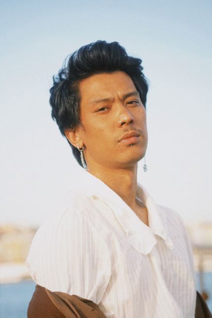 Portrait of a stylish young man with short hair wearing a white shirt, posing confidently outdoors.