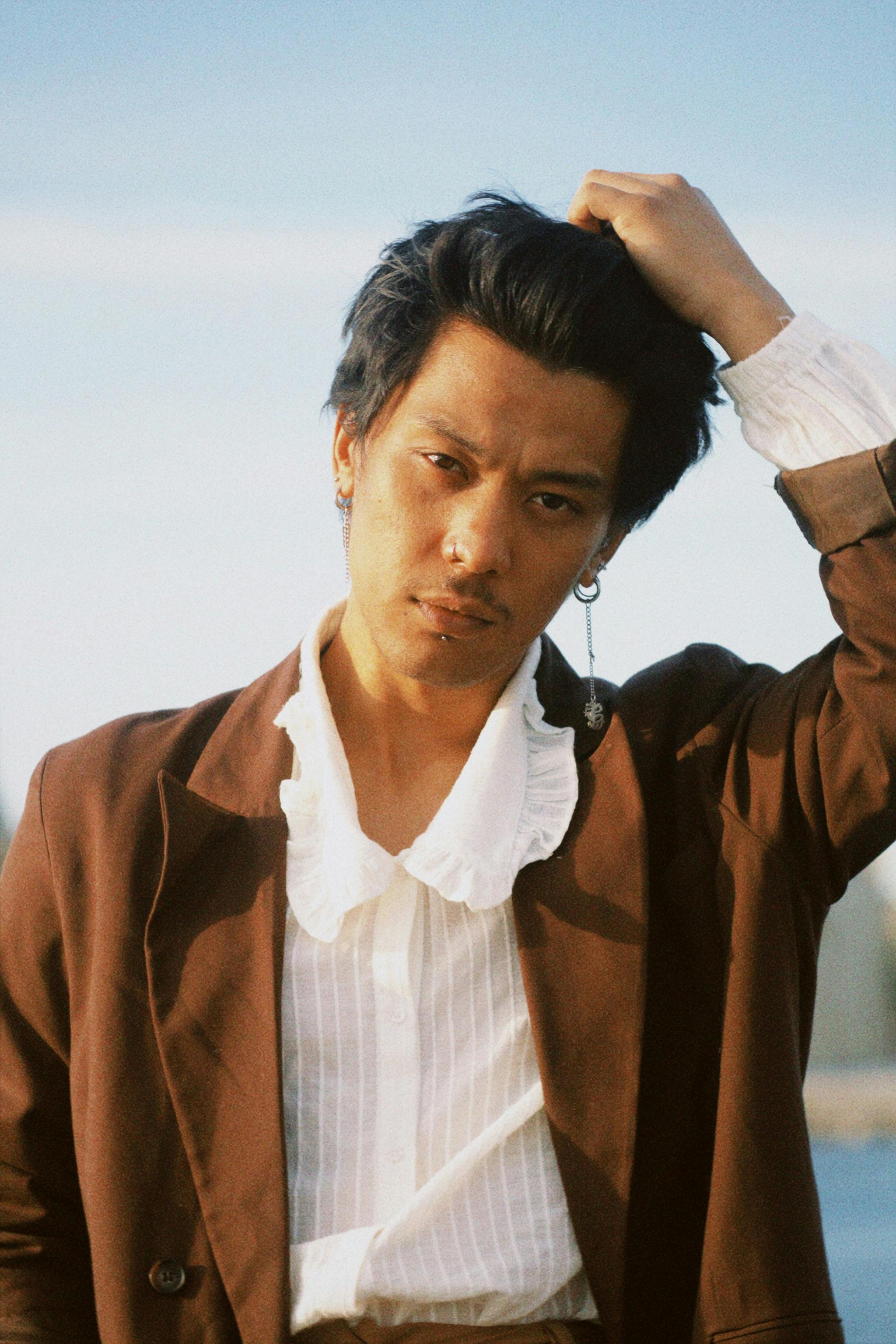 Fashionable young man with black hair wearing a brown suit posing outdoors. Captured in natural light with a stylish edge.