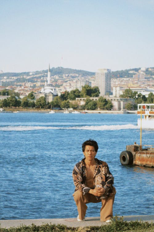 Man Crouching on River Bank Overlooking Istanbul Cityscape