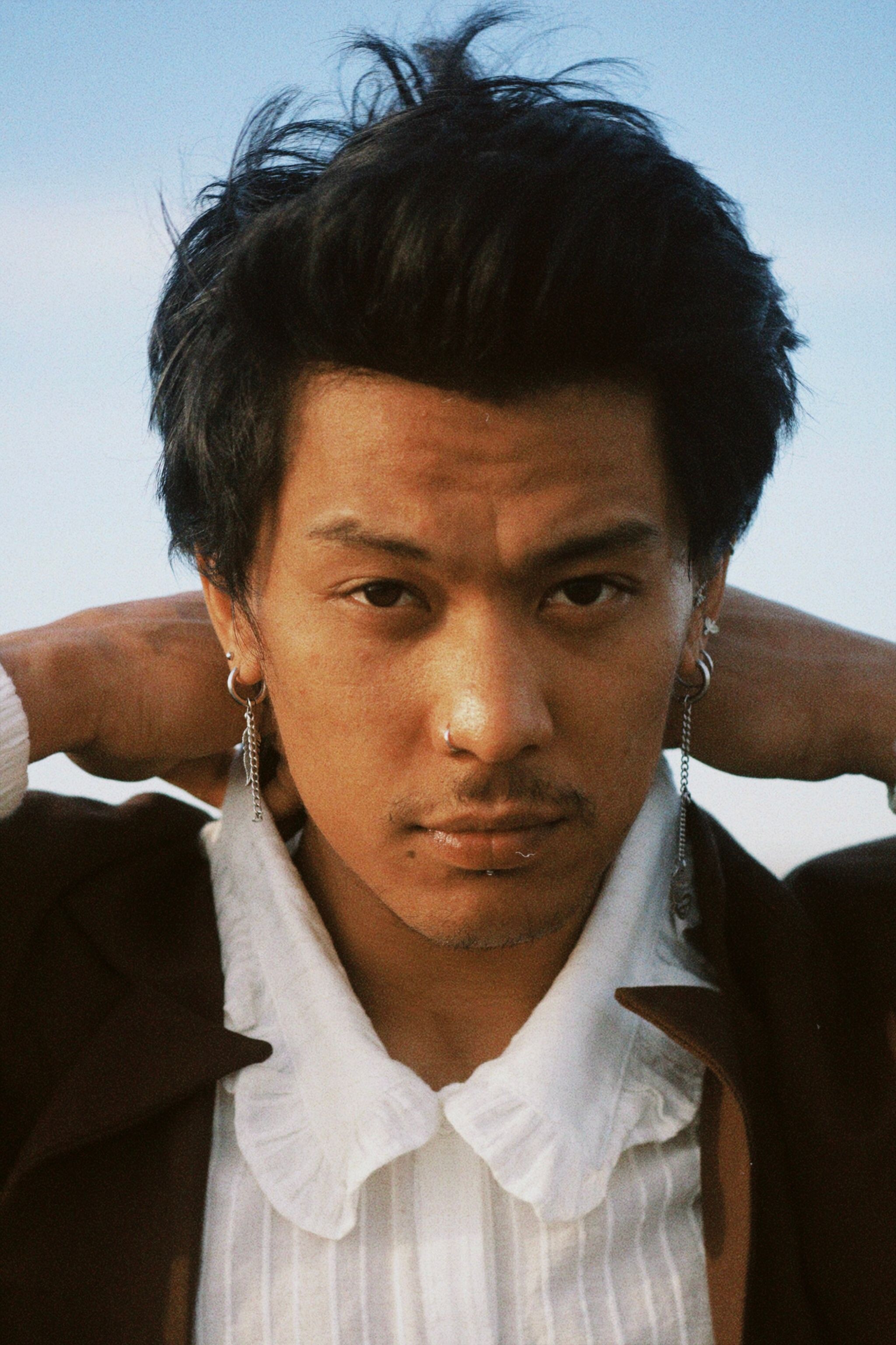 Stylish Asian man with black hair and earrings posing outdoors. Fashion portrait.