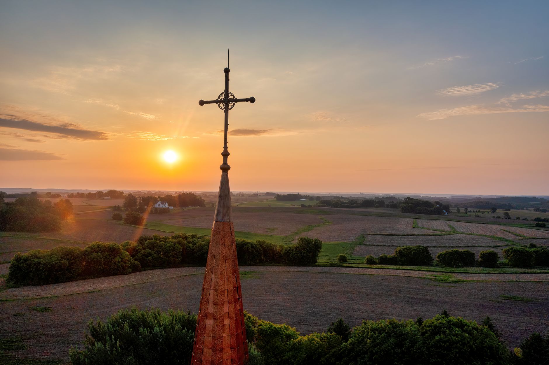 Sunset over rural countryside with a church spire in Lund, Wisconsin, highlighting faith and tranquility.