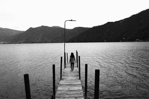 Woman Walking on Wooden Pier in Black and White