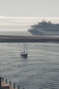 A serene view of a large cruise liner passing by a small sailboat on a calm sea day.