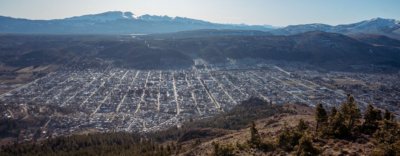 A sweeping aerial view of a city nestled in a mountainous landscape, showcasing a grid pattern with serene surroundings.