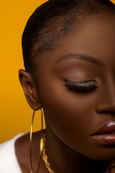 Close-up portrait of a woman with gold hoop earring against a vibrant yellow background.