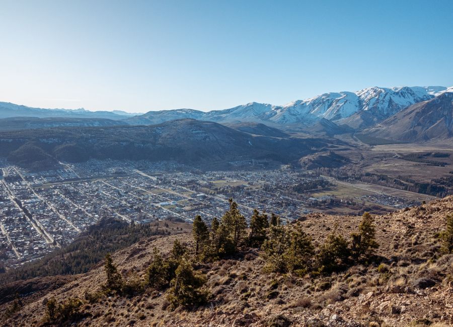 A breathtaking panoramic view of Esquel, Argentina, with snow-capped mountains and clear blue skies.