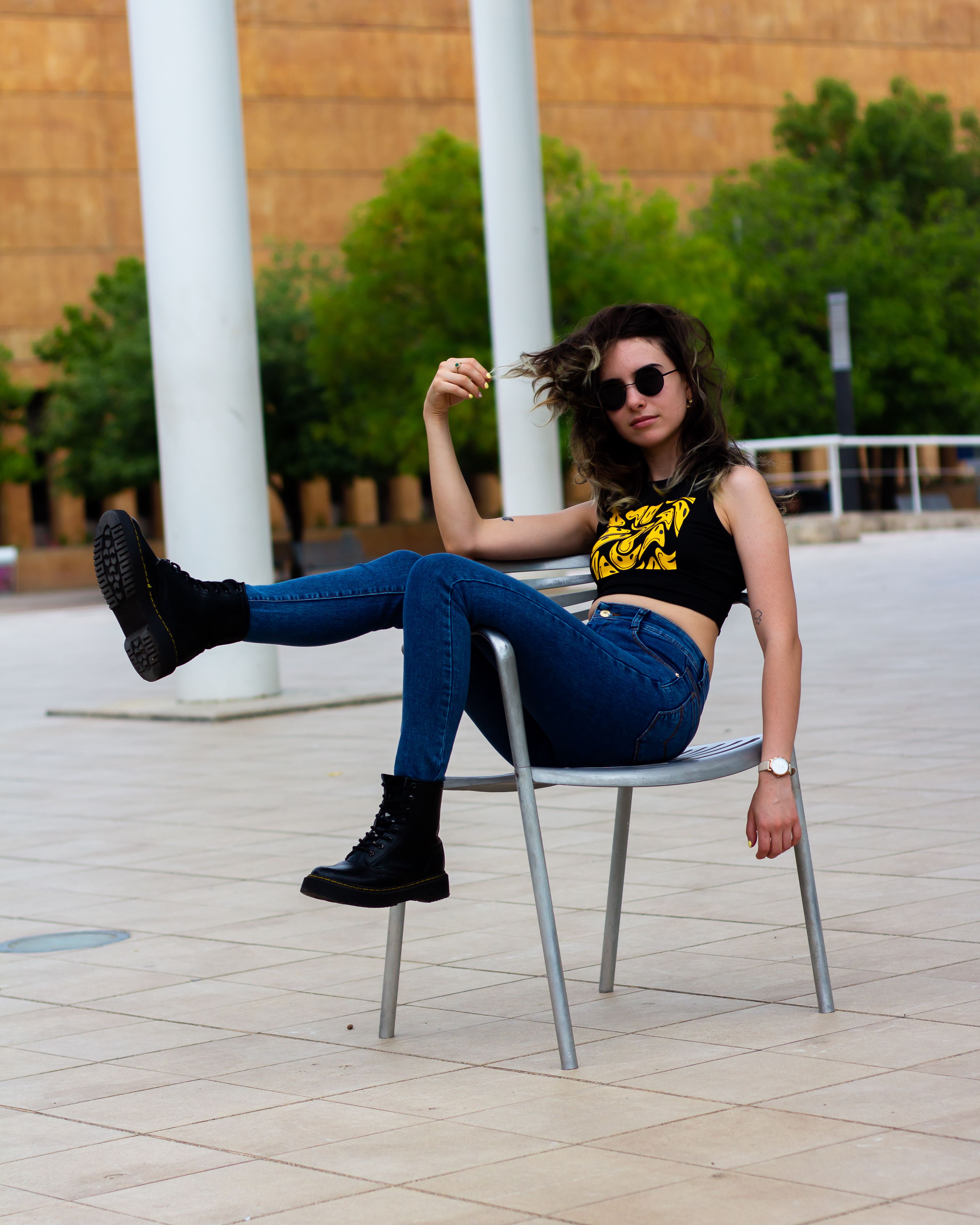 Young Woman in a Tank Top and Jeans Sitting on a Chair and Playing with ...